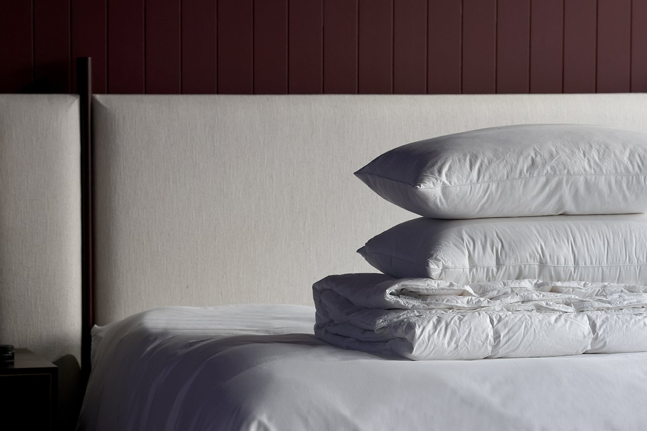 Luxury white And So To Bed bedding, goose down duvets and pillows neatly sat on top of a dressed mattress, behind sits a white, custom-made Vispring headboard